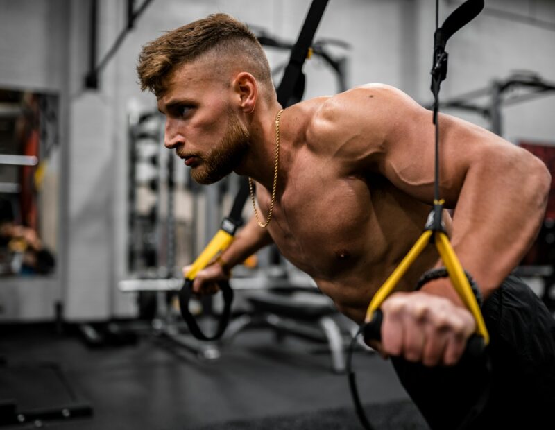 topless man in black pants holding black and yellow exercise equipment