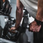 person in gray shirt holding black dumbbell