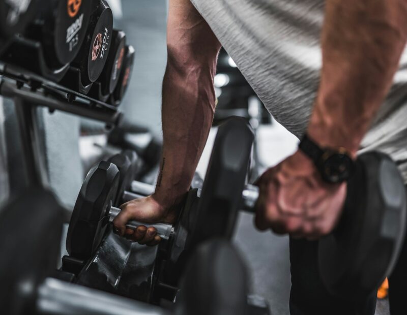 person in gray shirt holding black dumbbell